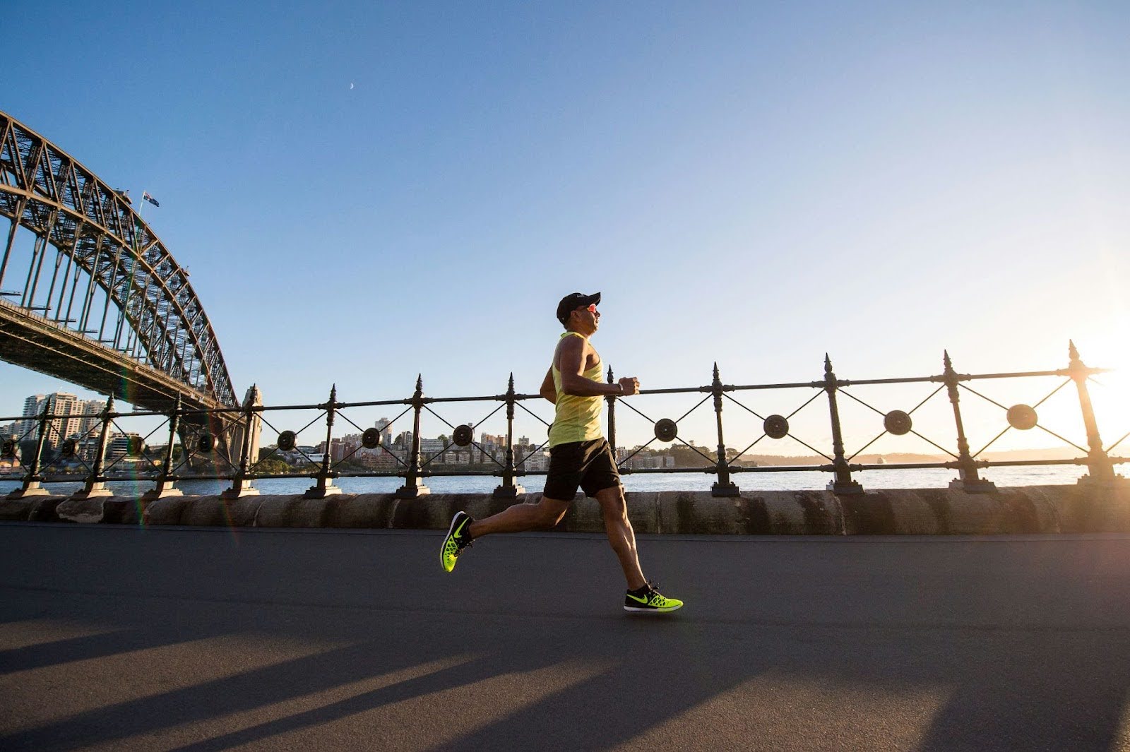 Runner jogging alongside a river with a bridge and city skyline in the background