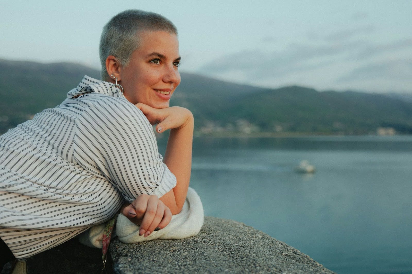 Woman with short hair leaning on a railing overlooking a lake