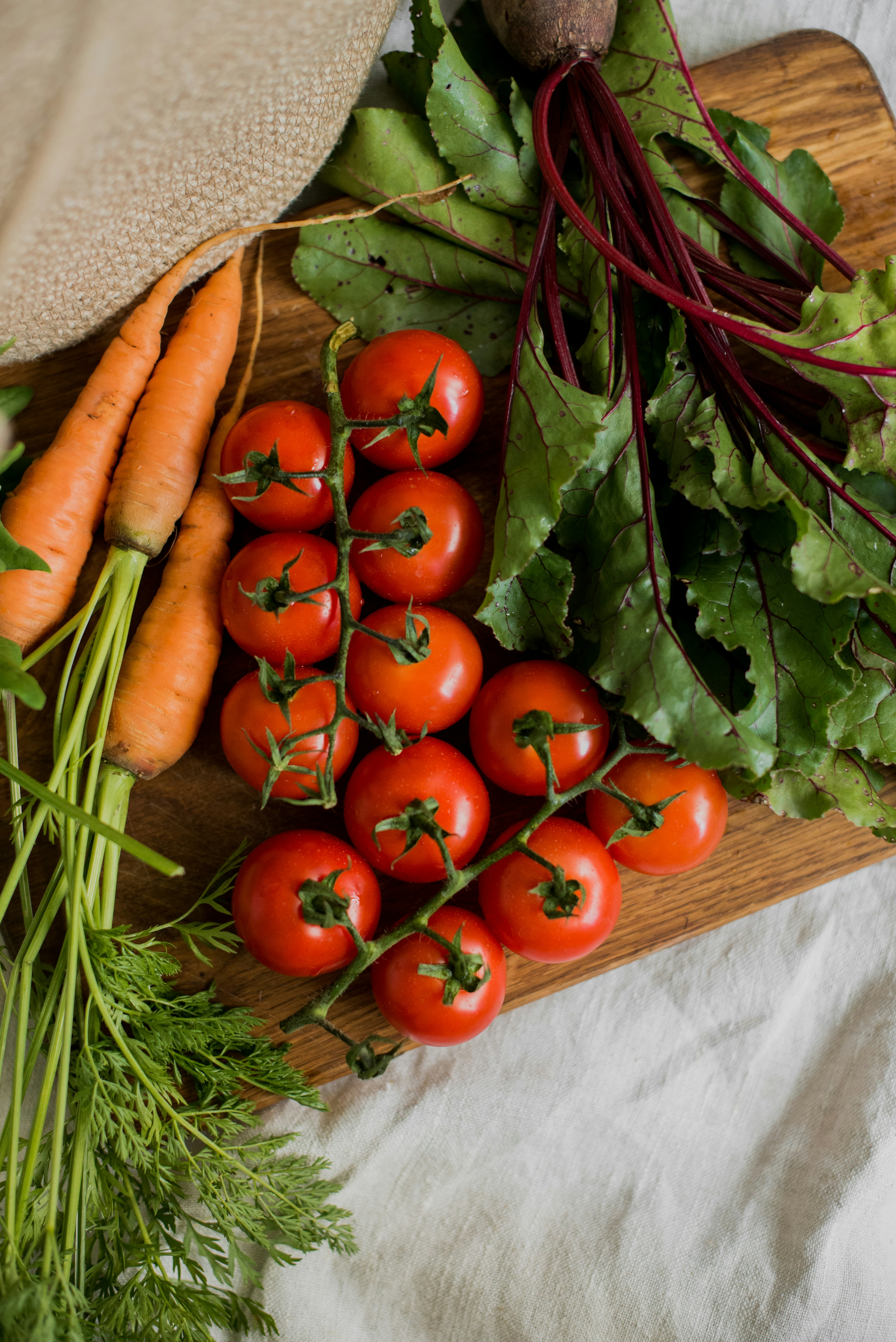 Carrots, tomatoes, and beets arranged on a wooden cutting board
