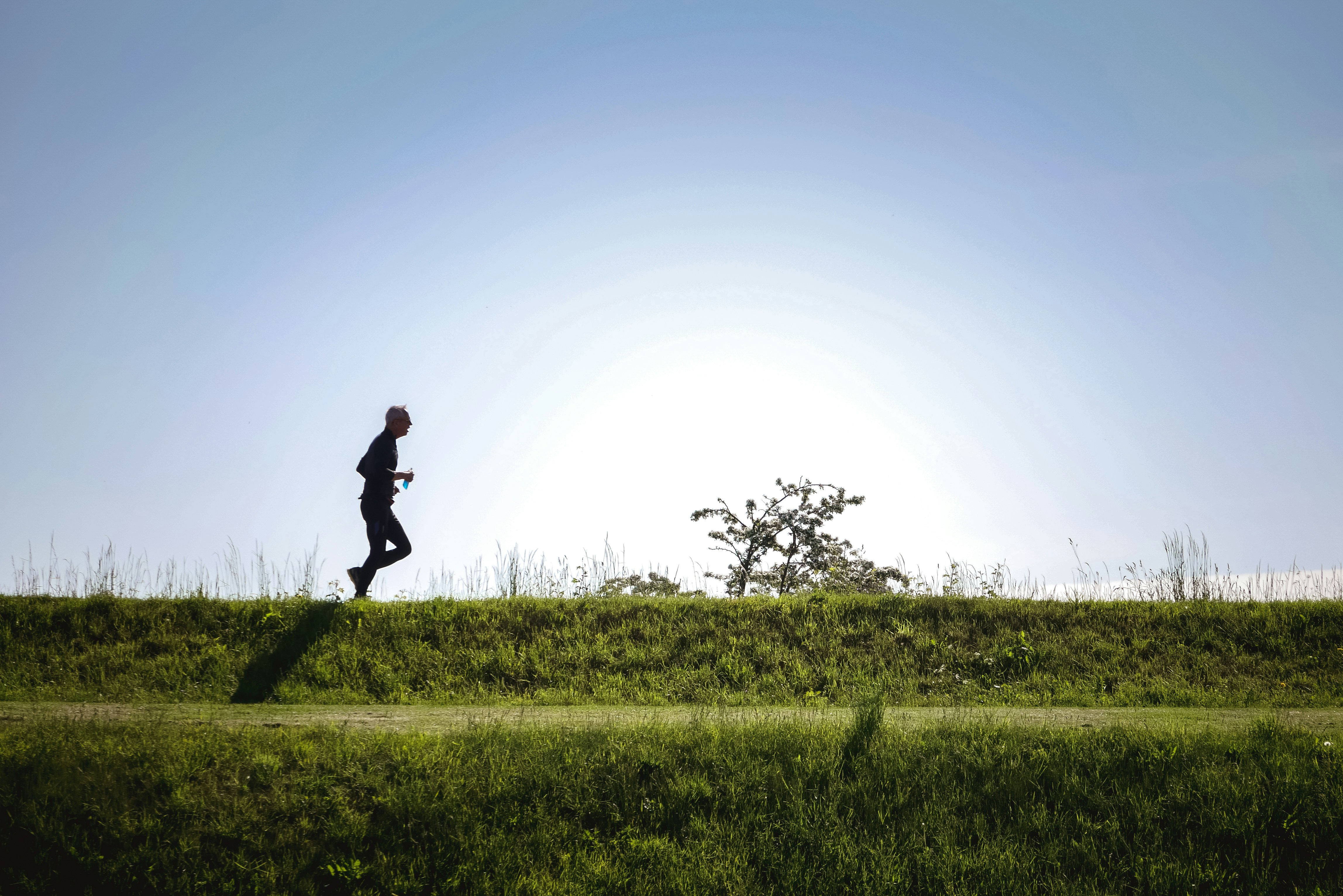 Older man jogging through a green field while holding a water bottle