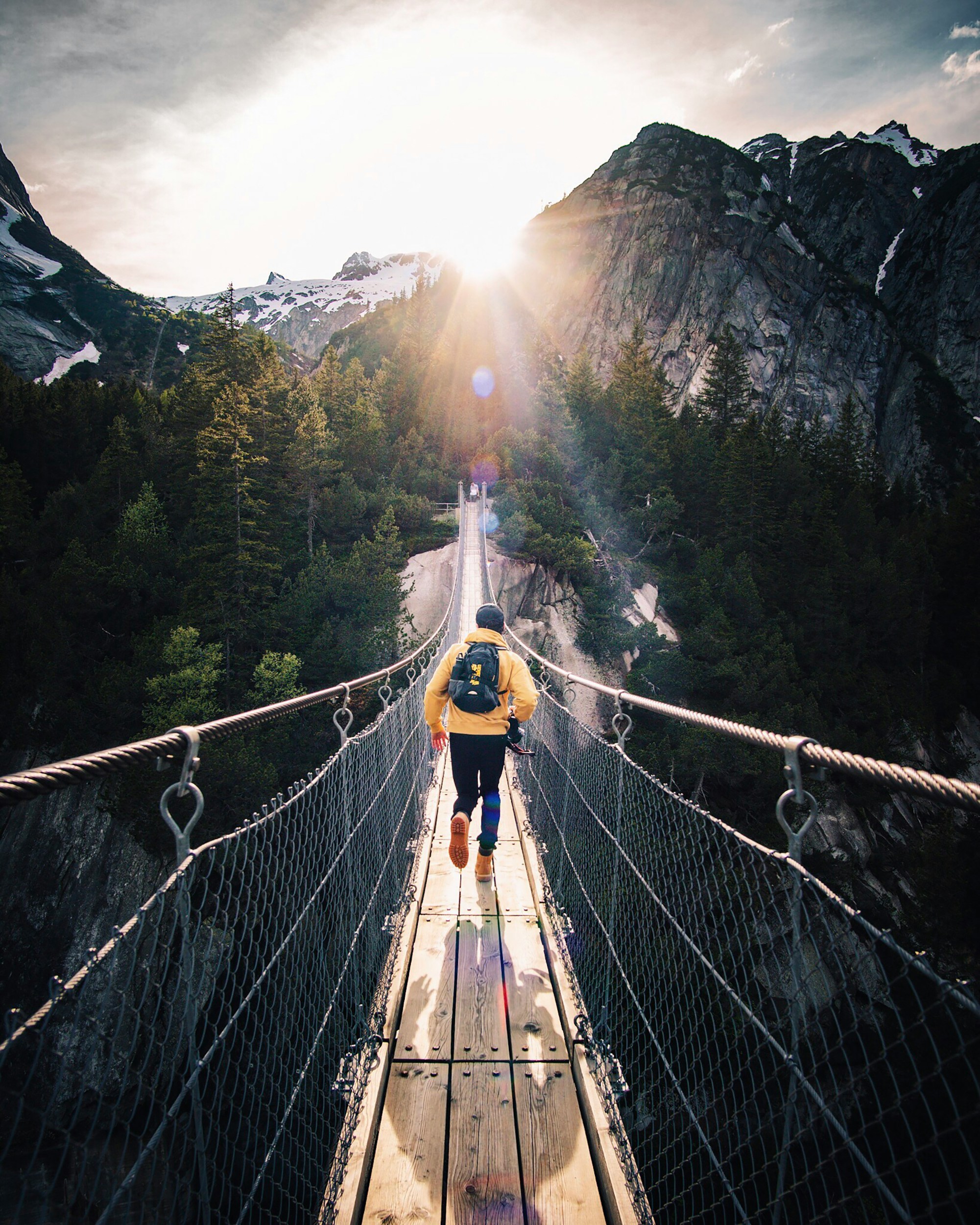Person crossing a pedestrian suspension bridge in a mountain setting
