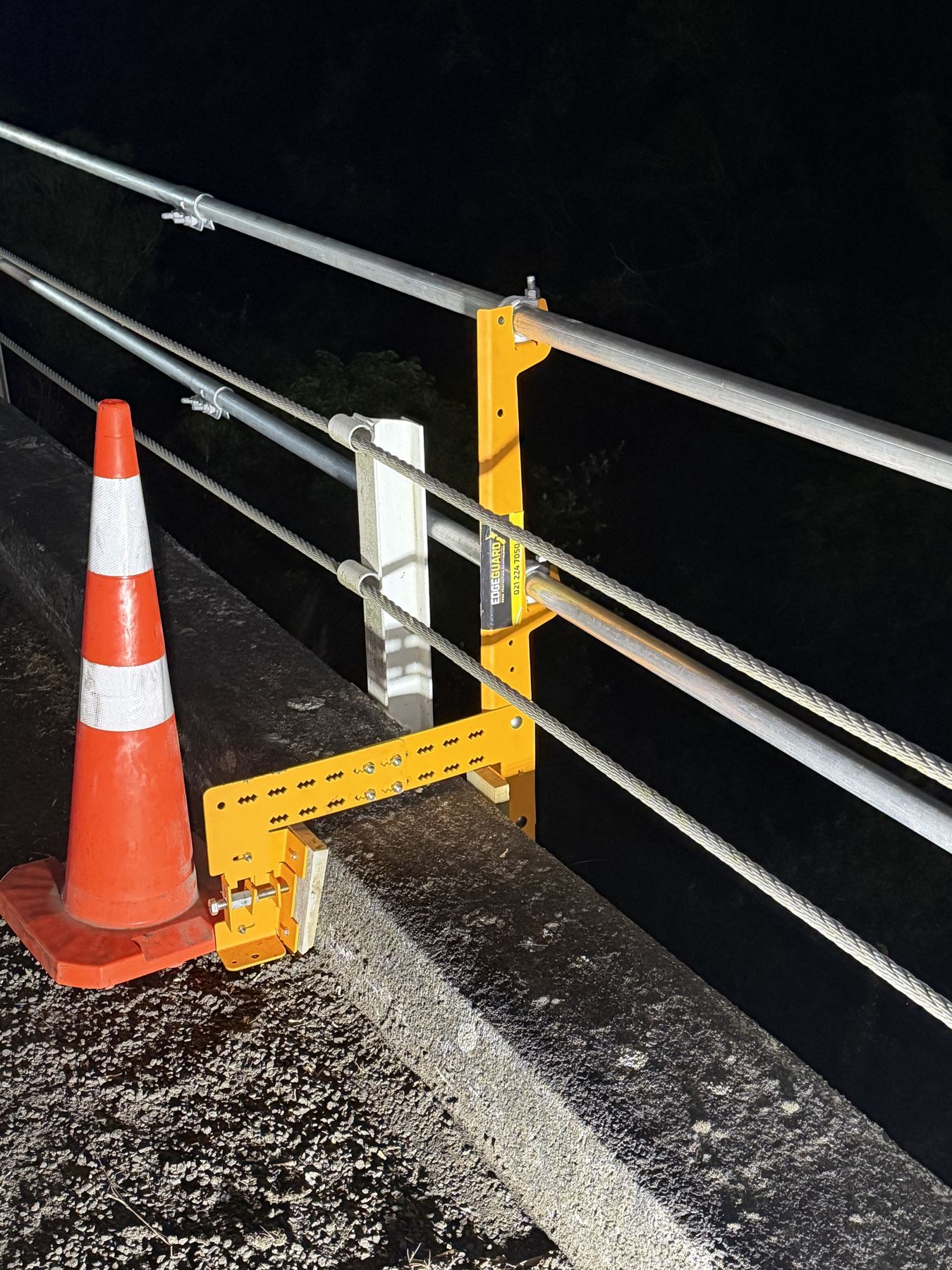 EdgeGuard clamp bracket gripping an existing concrete roadside barrier with guardrail fitted