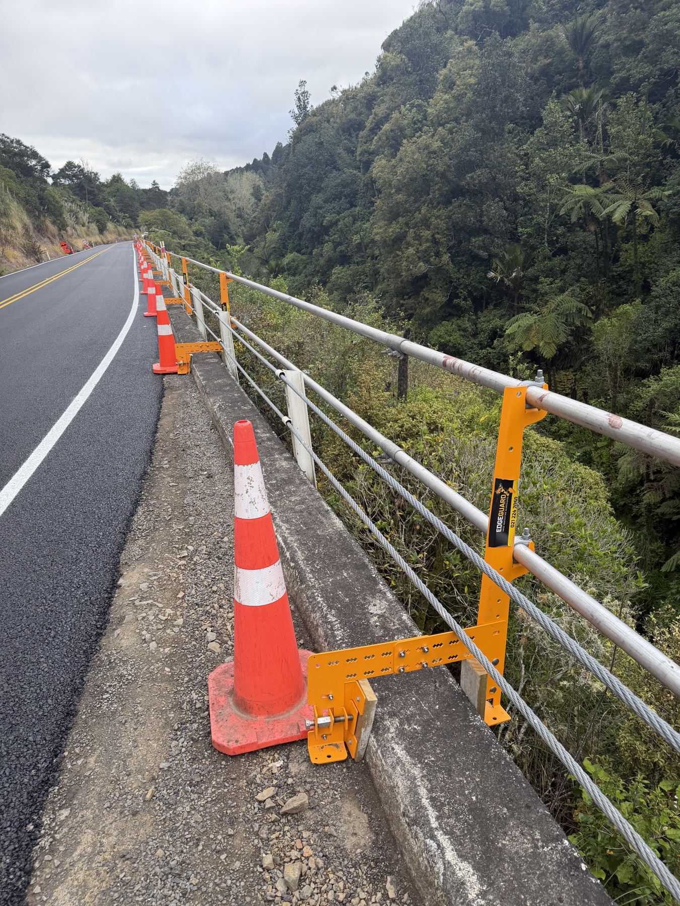 EdgeGuard clamp bracket fixed to a concrete roadside barrier above a gorge