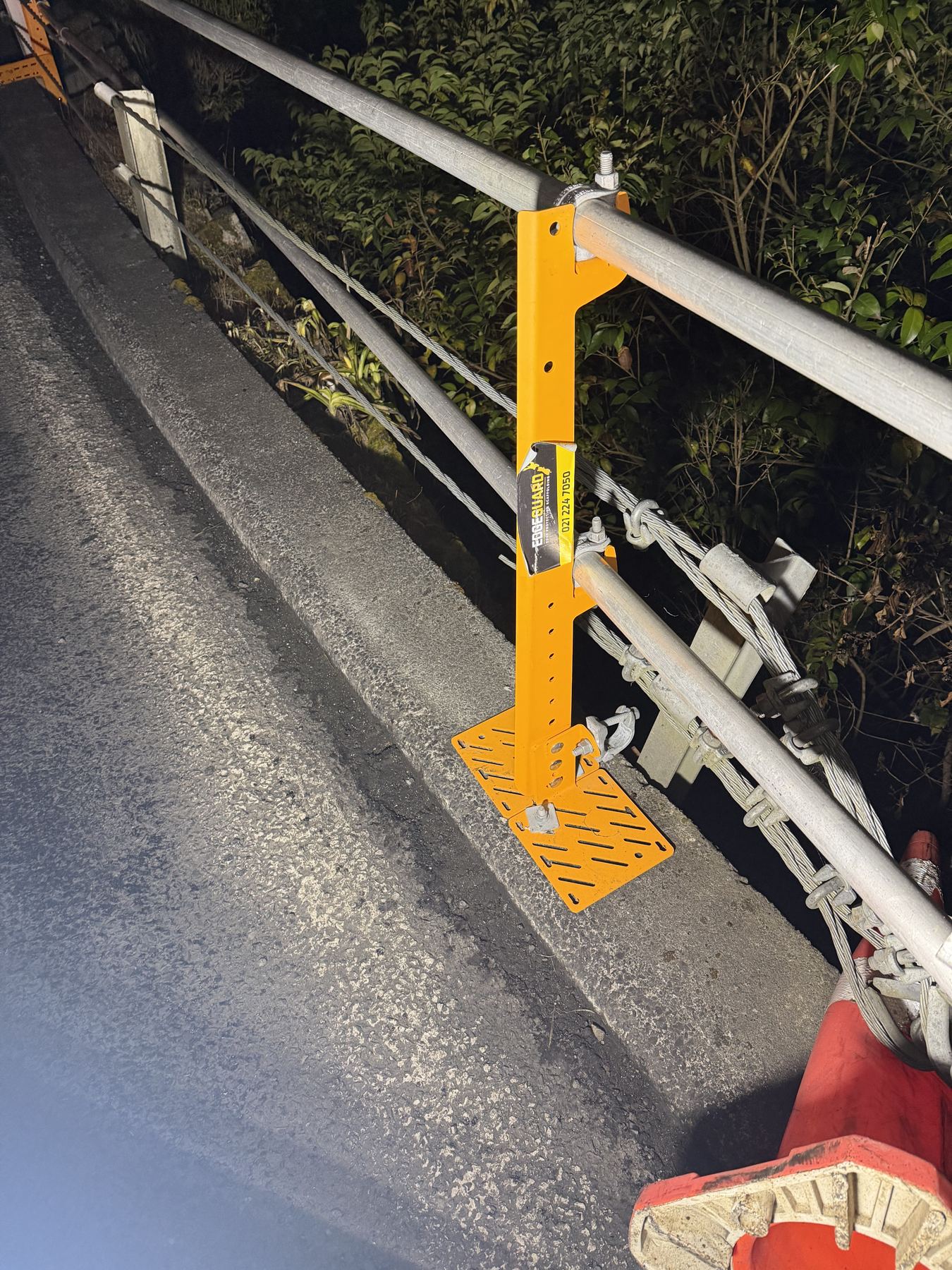 EdgeGuard direct-fix bracket anchored to the top of a concrete roadside barrier