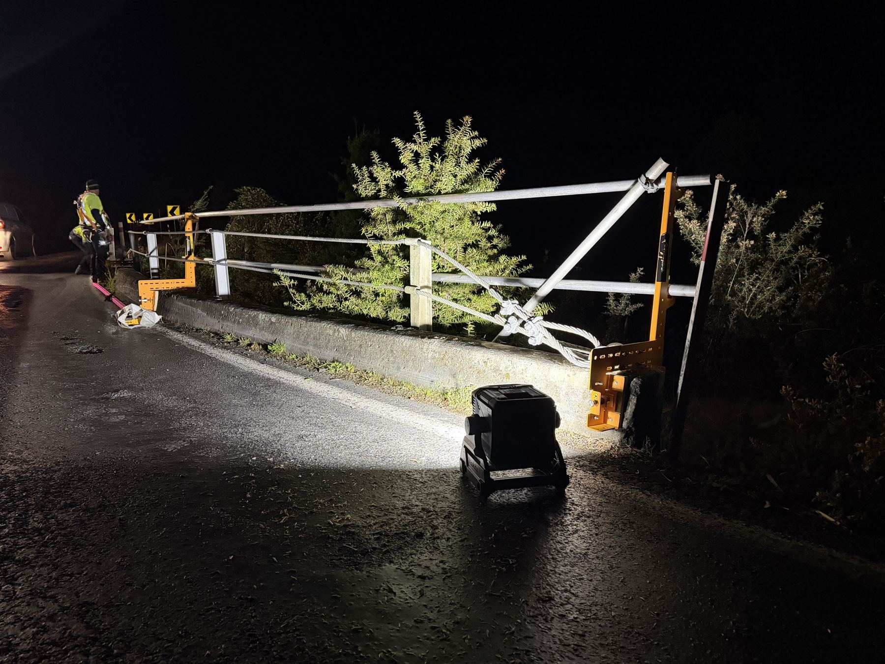 Guardrail being fitted to a roadside concrete barrier at night