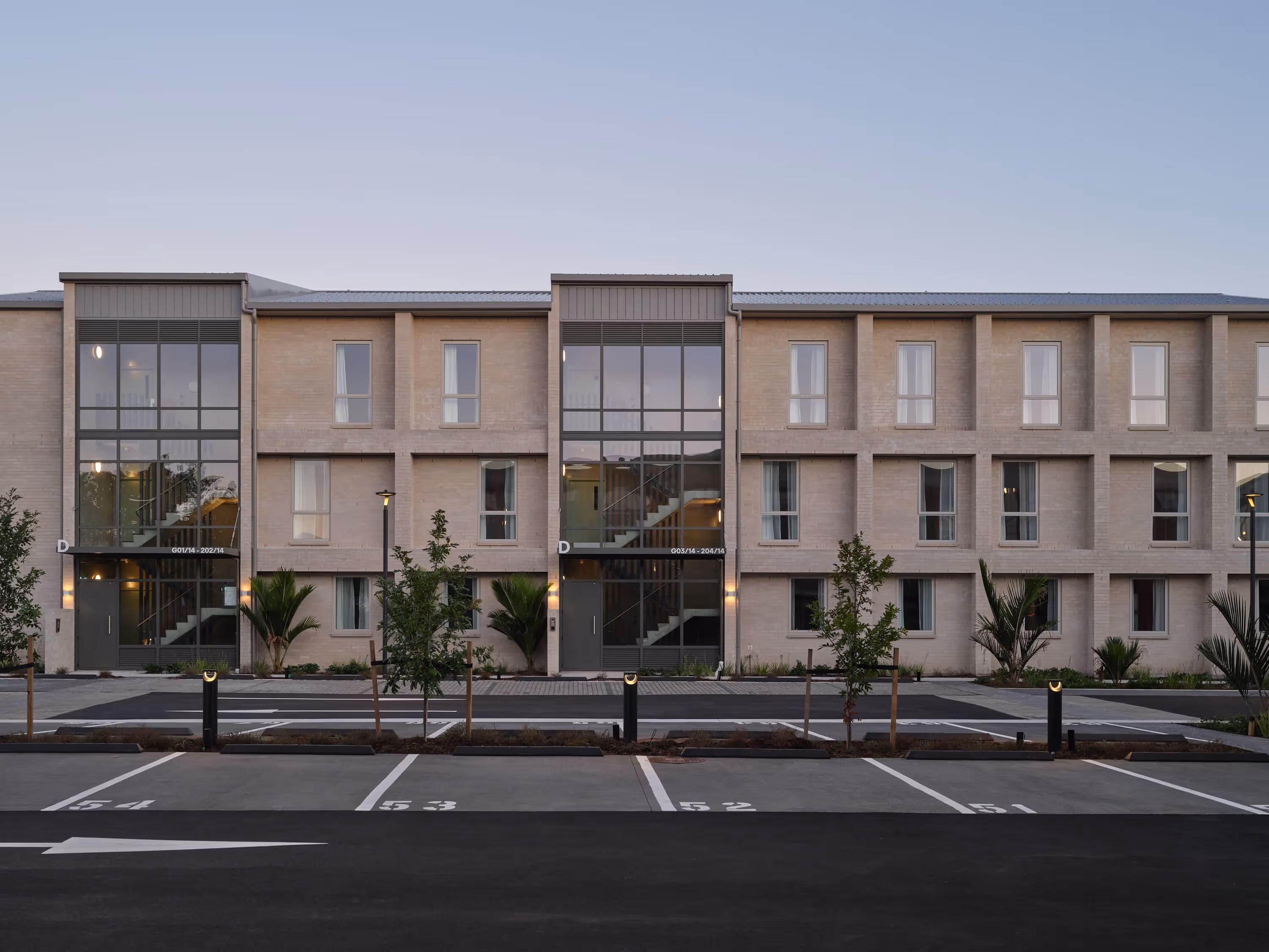 Modern three-story apartment building with large windows and numbered parking spaces in front.