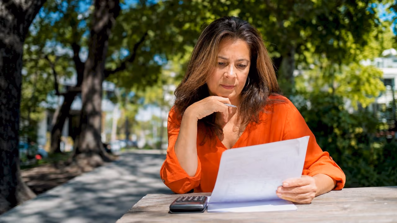 Una mujer revisa sus cuentas mientras consulta la calculadora y analiza sus documentos financieros.