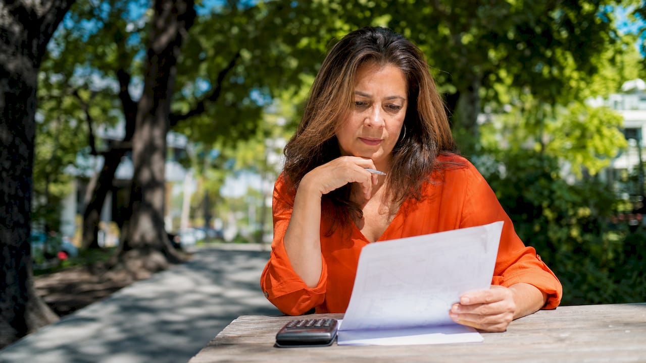 Una mujer revisa sus cuentas mientras consulta la calculadora y analiza sus documentos financieros.