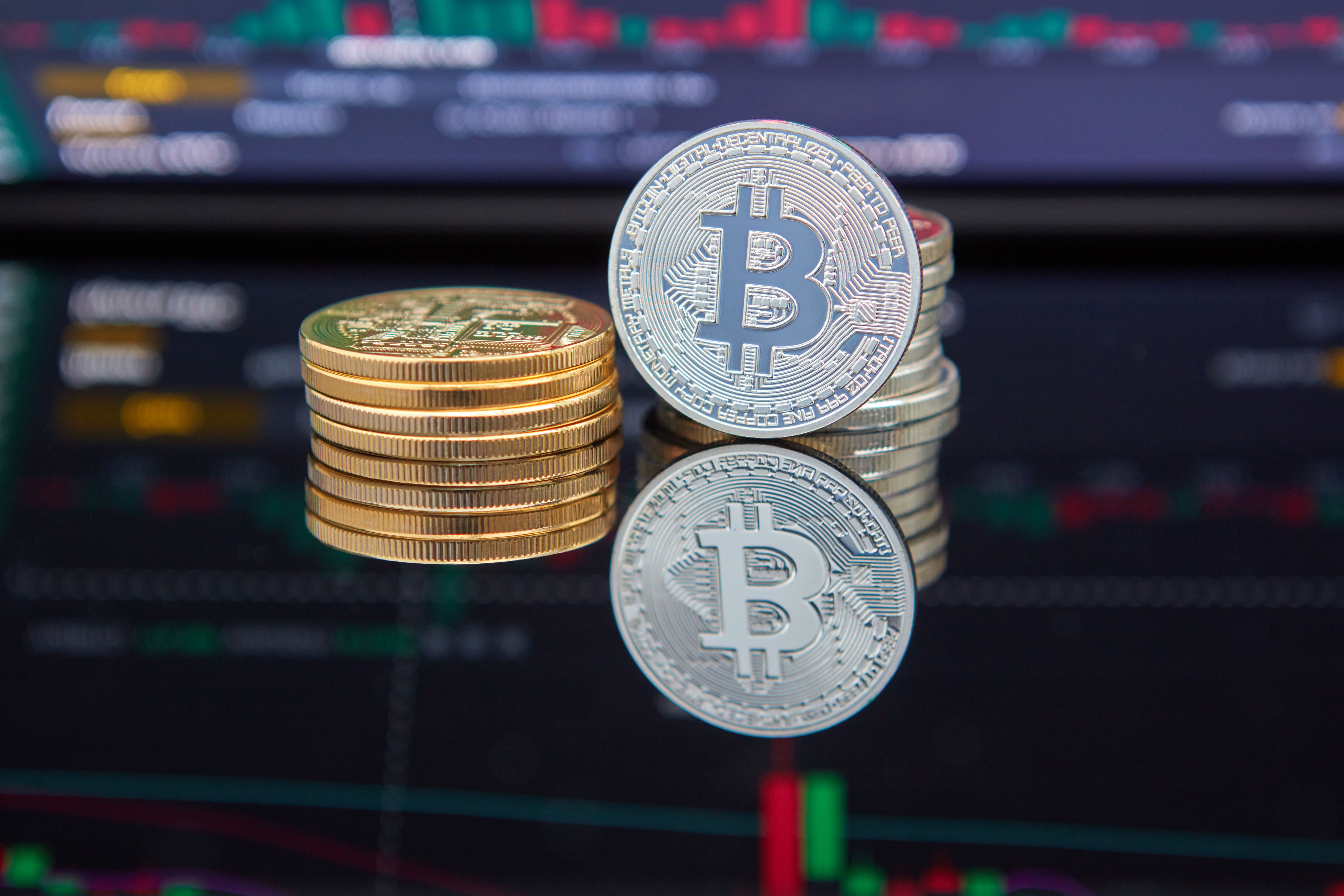Monedas de bitcoin apiladas frente a una pantalla con un gráfico de trading de criptomonedas