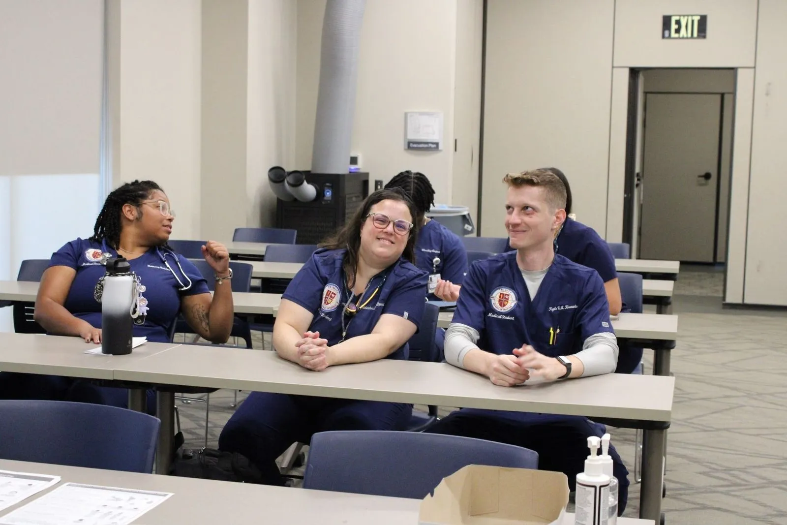 Three student sitting at a desk waiting for instruction to begin.