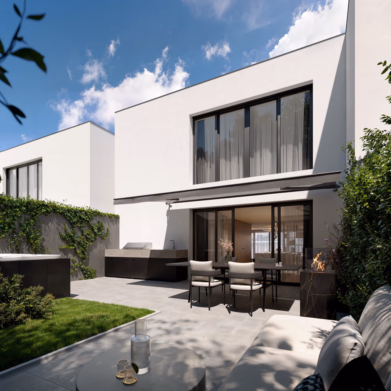 Modern white two-story house with large windows, outdoor dining area, greenery, and partly cloudy blue sky.