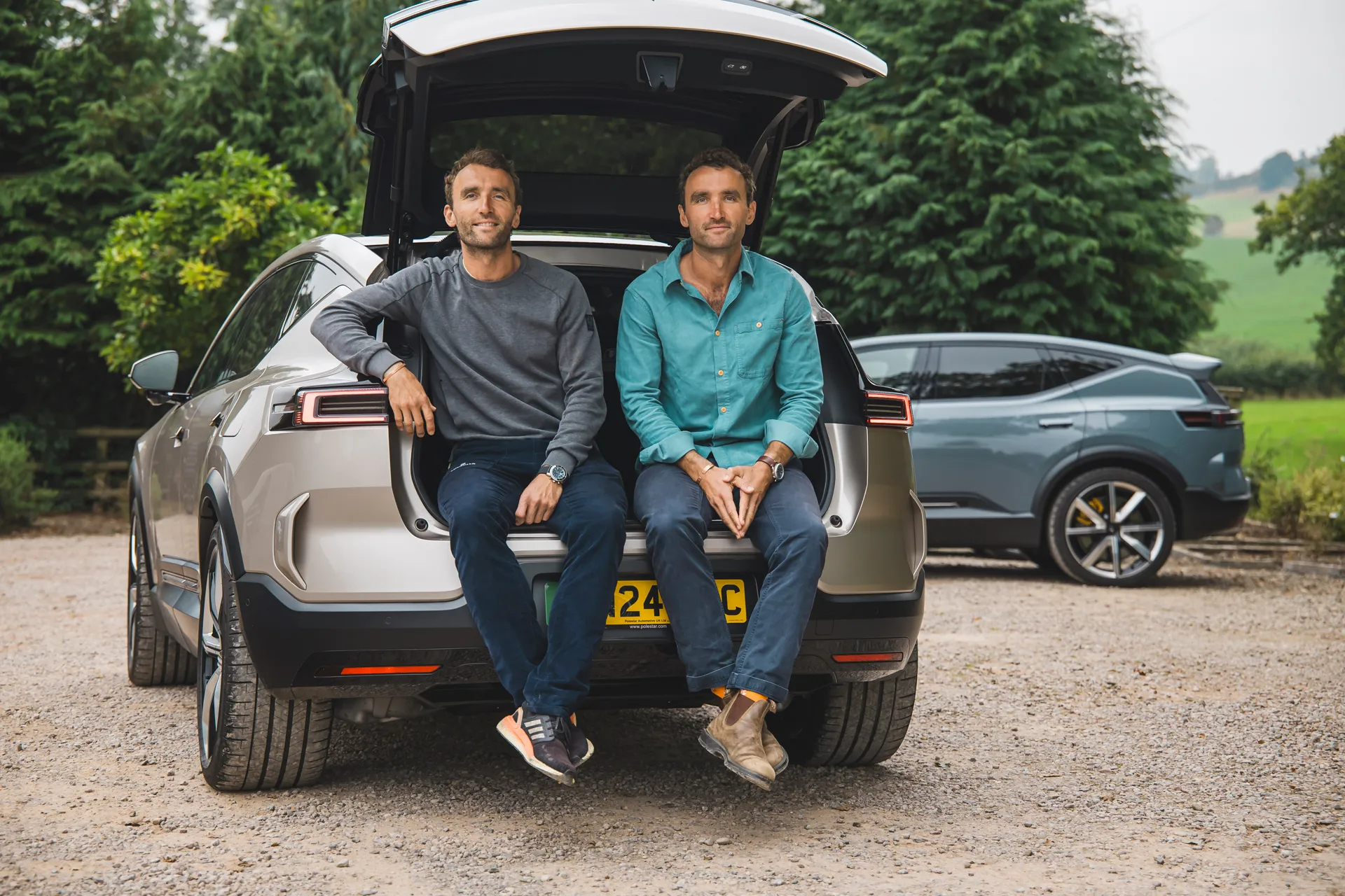The Turner Twins sitting in the open boot of an electric car in the countryside