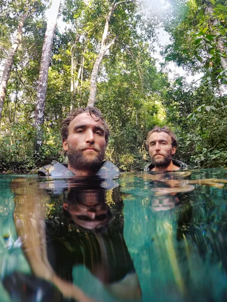 The Turner Twins up to their necks in clear water in a tropical forest