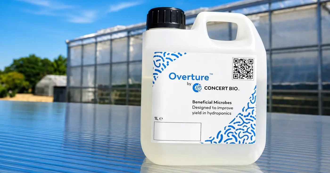 A 1 litre bottle of Overture beneficial microbes in front of a greenhouse