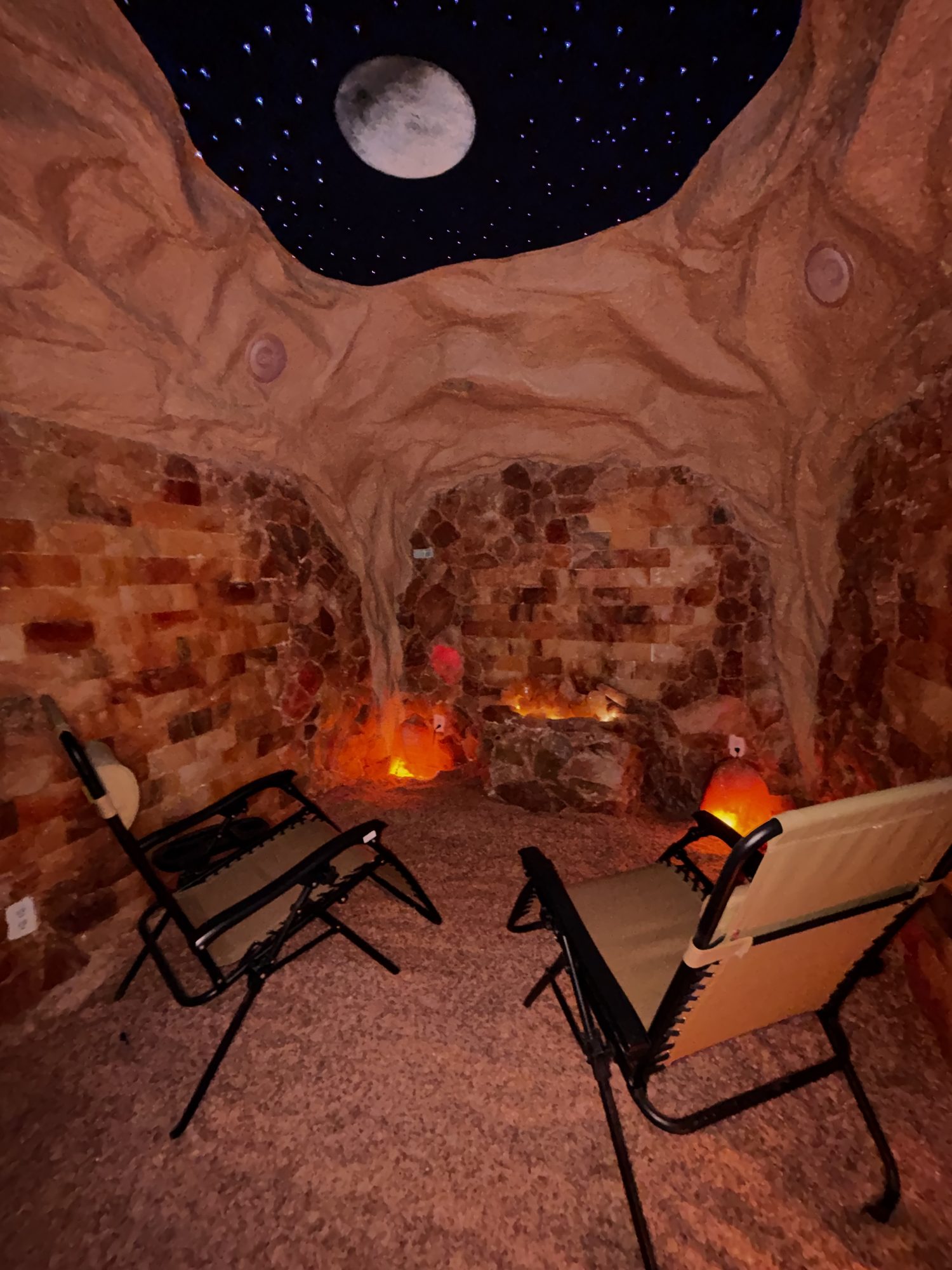 Two zero-gravity chairs on a salt floor under a starry night ceiling in the Altered States salt cave