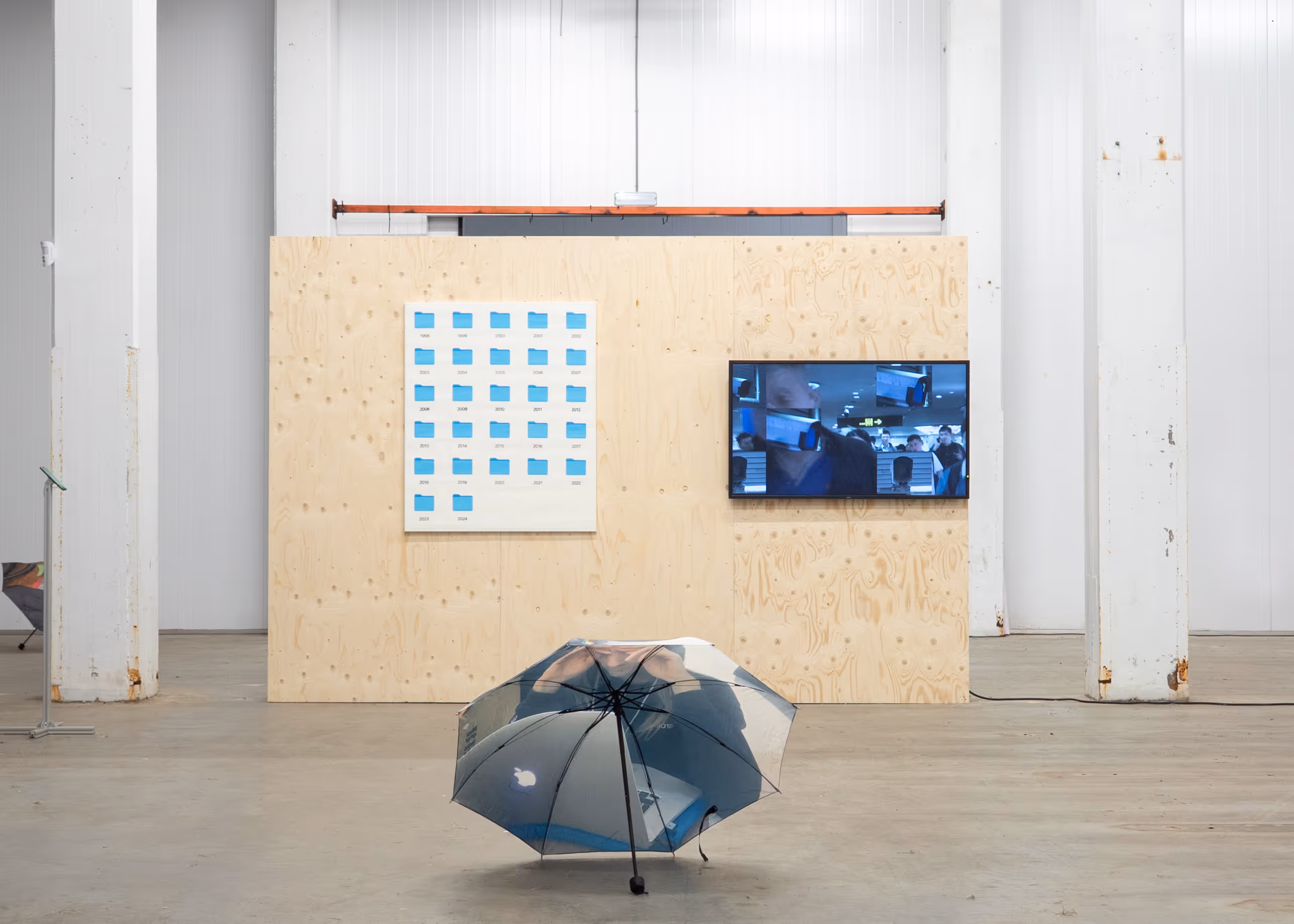 Exorcise the Candy House exhibition view with video screen, symbolic folder artwork, and umbrella installation at Katoenhuis.