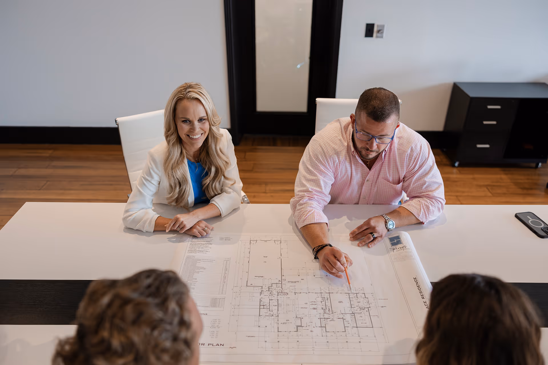 Stephanie and Ray Hubner sitting at a table with a client, reviewing blueprints and discussing the home selling process.