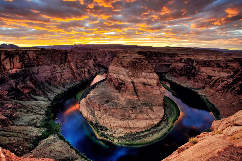 Sunset over Horseshoe Bend with a winding river carving through steep red rock canyon walls.