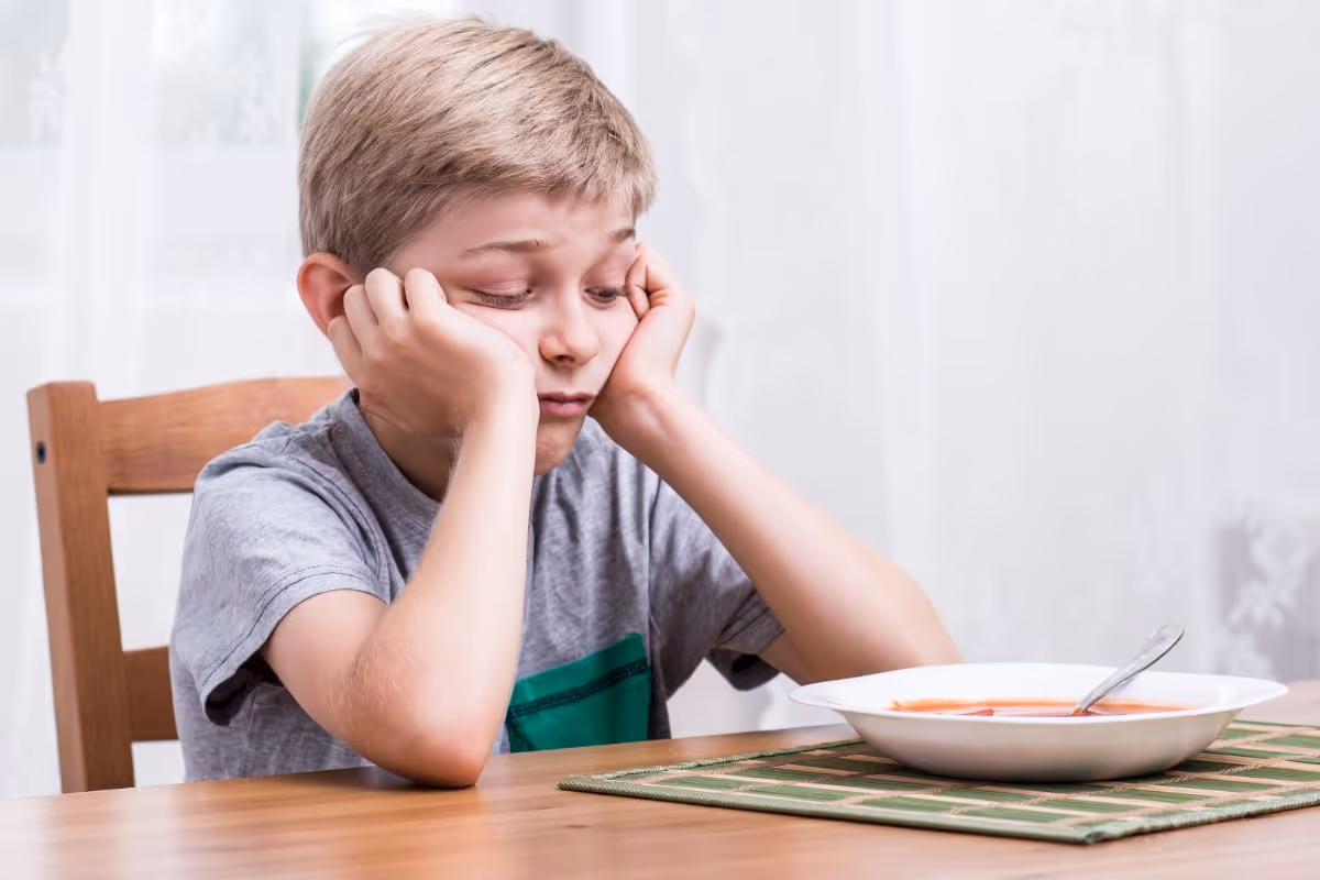 child sitting at the dining table looking sadly at a bowl of food