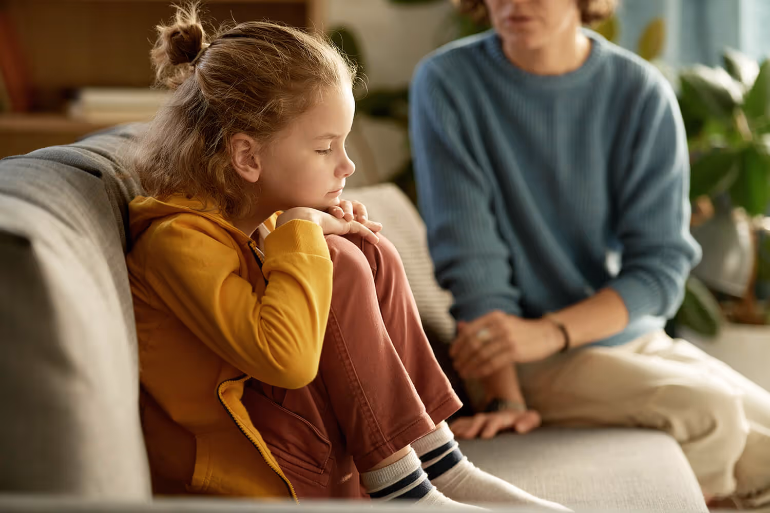 a child sitting on a coach looking anxious while a parent sits next to them in the background