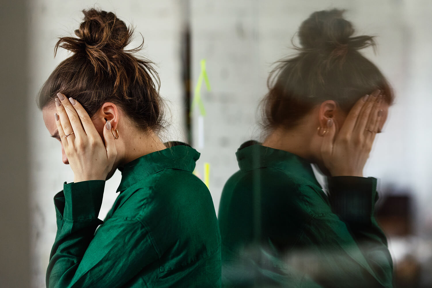 An anxious woman in a green shirt holding her face in her hands, reflecting perfectionism and mental exhaustion.