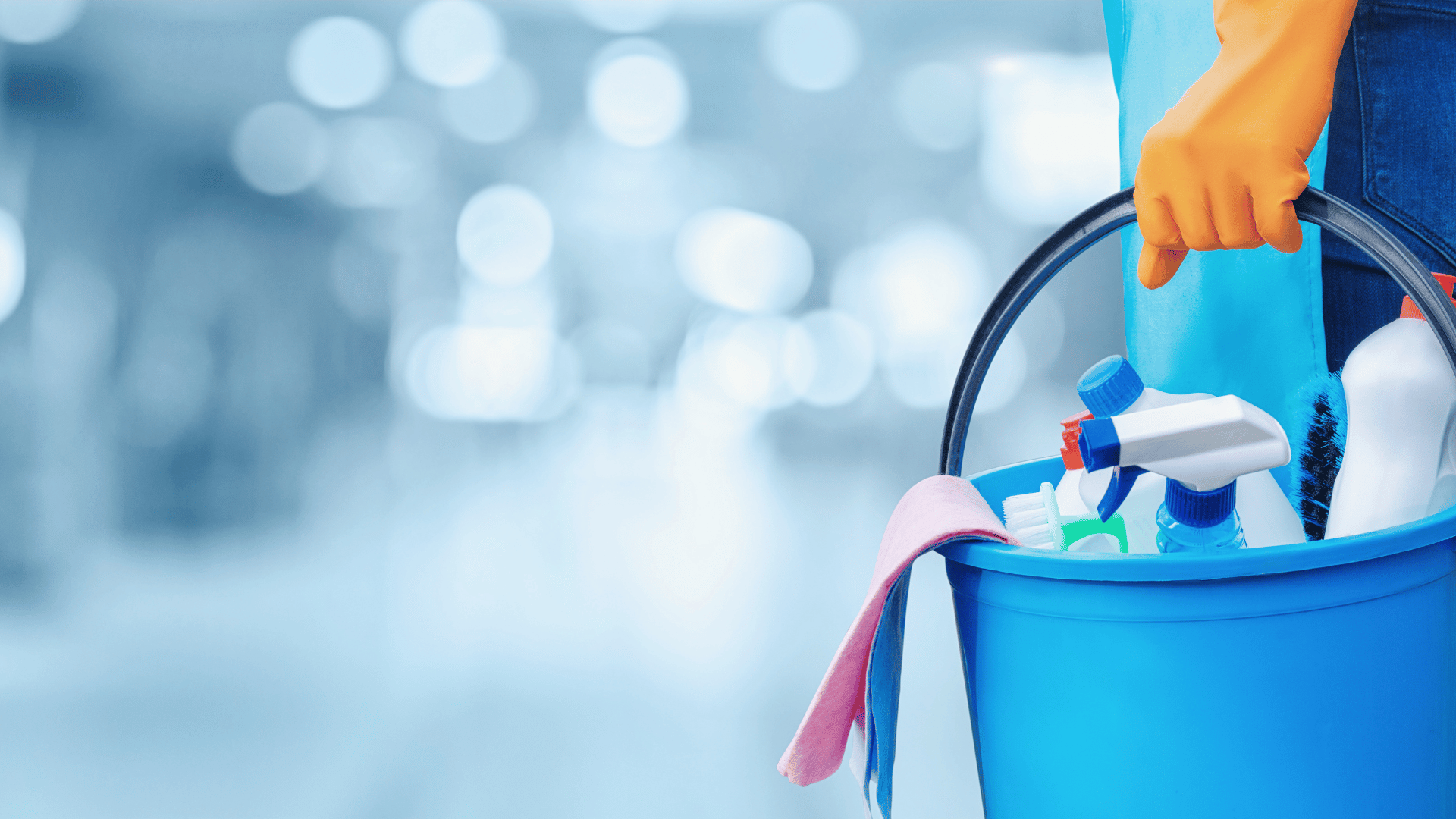 A person stands holding a bucket filled with various cleaning supplies, ready to tackle household chores.
