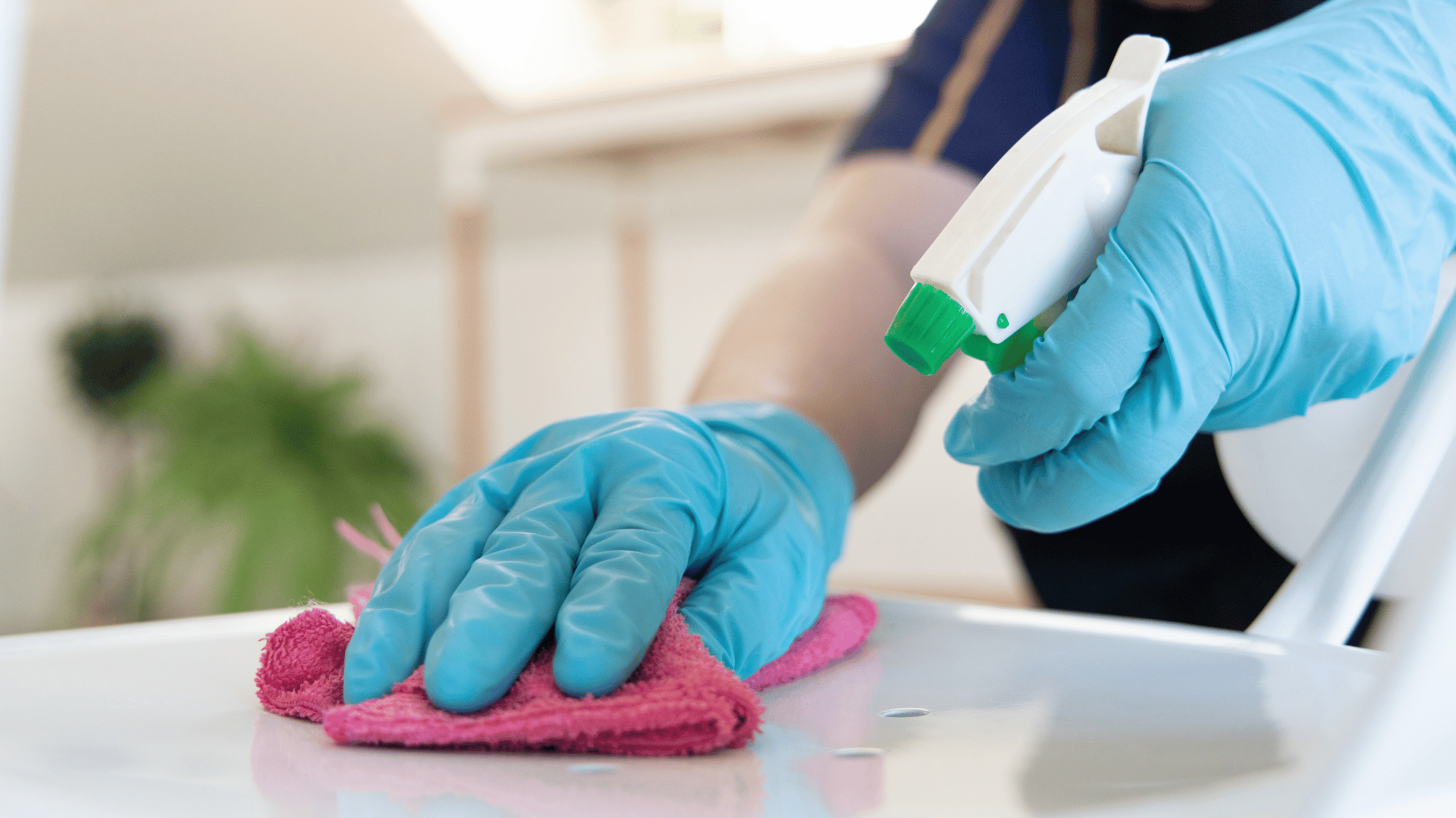 A person wearing blue gloves is diligently cleaning a white table, ensuring a spotless surface.