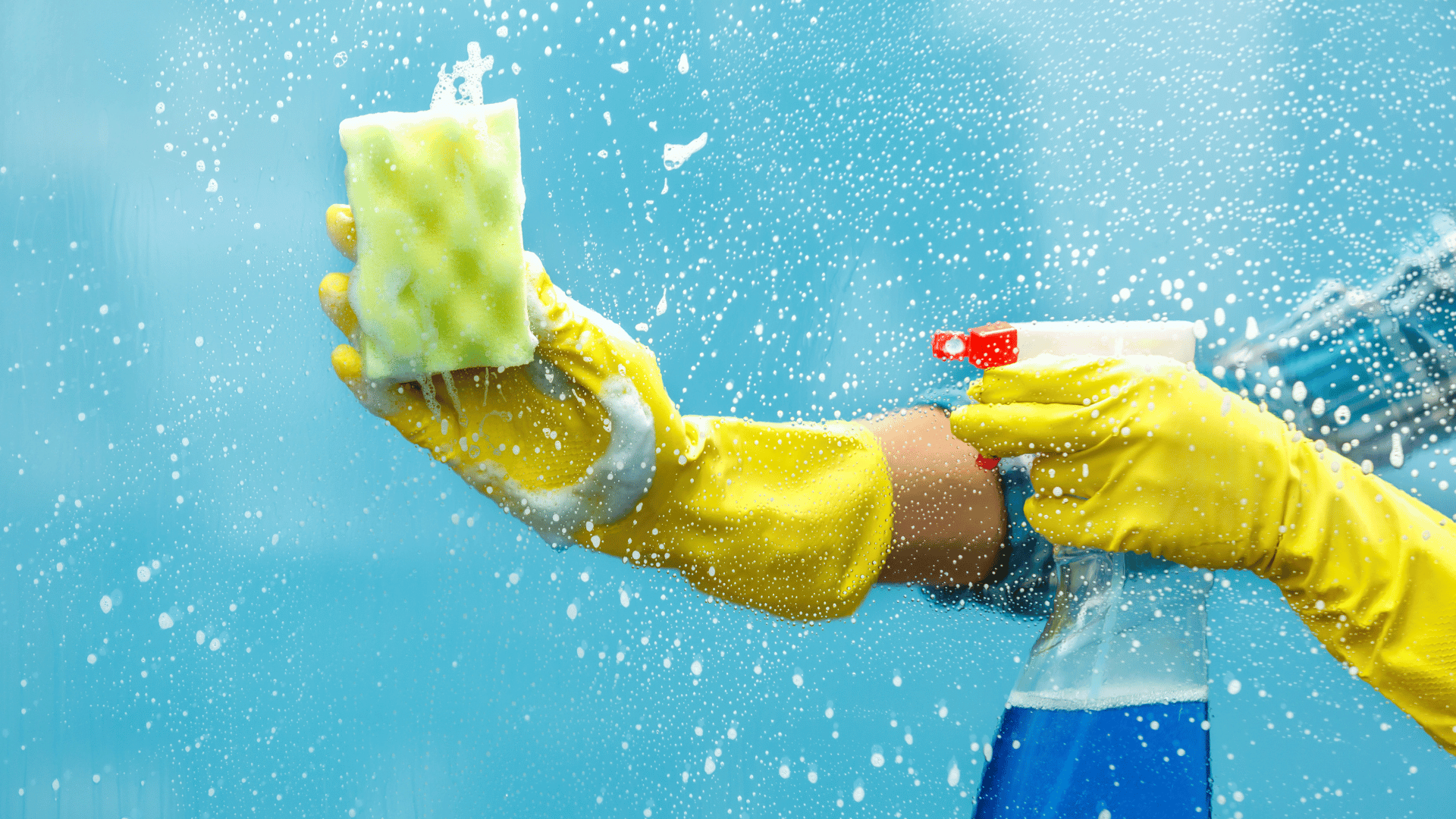 A person wearing yellow rubber gloves cleans a window with a sponge, demonstrating effective cleaning techniques.