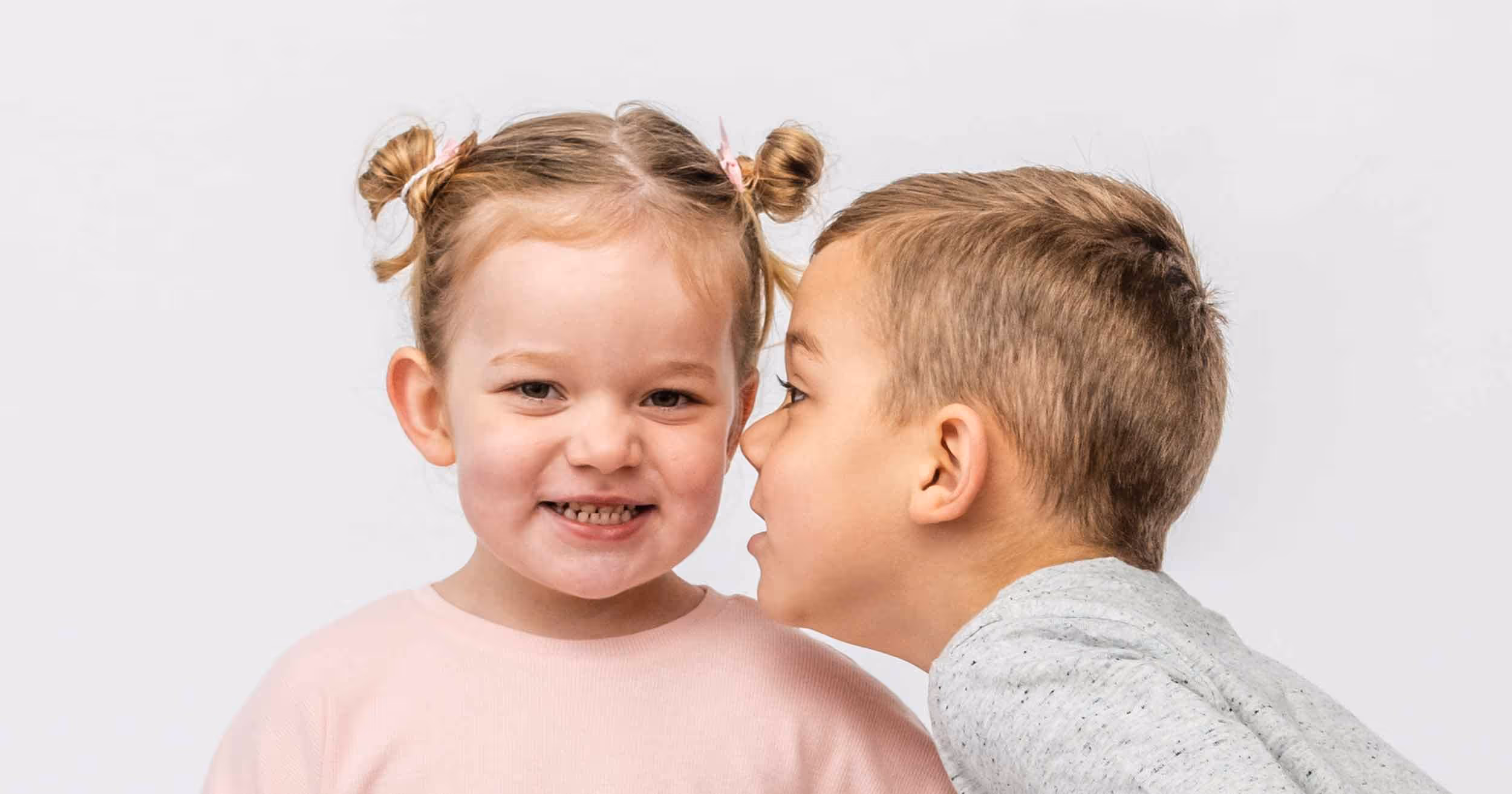 5 year old boy whispering into the ear of his 3 year old sister