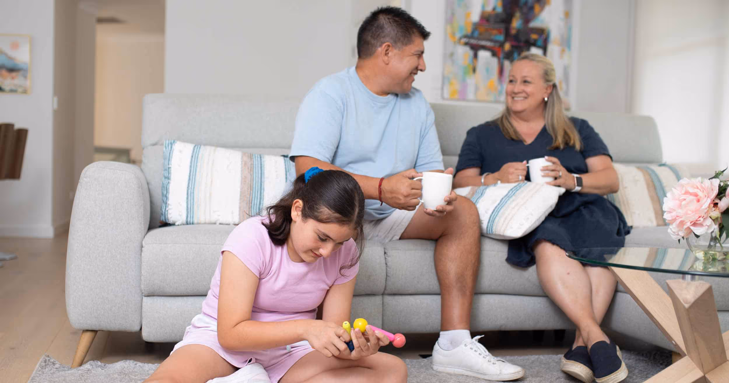 parents sitting on couch drinking coffee talking to each other while teenage girl plays on the floor