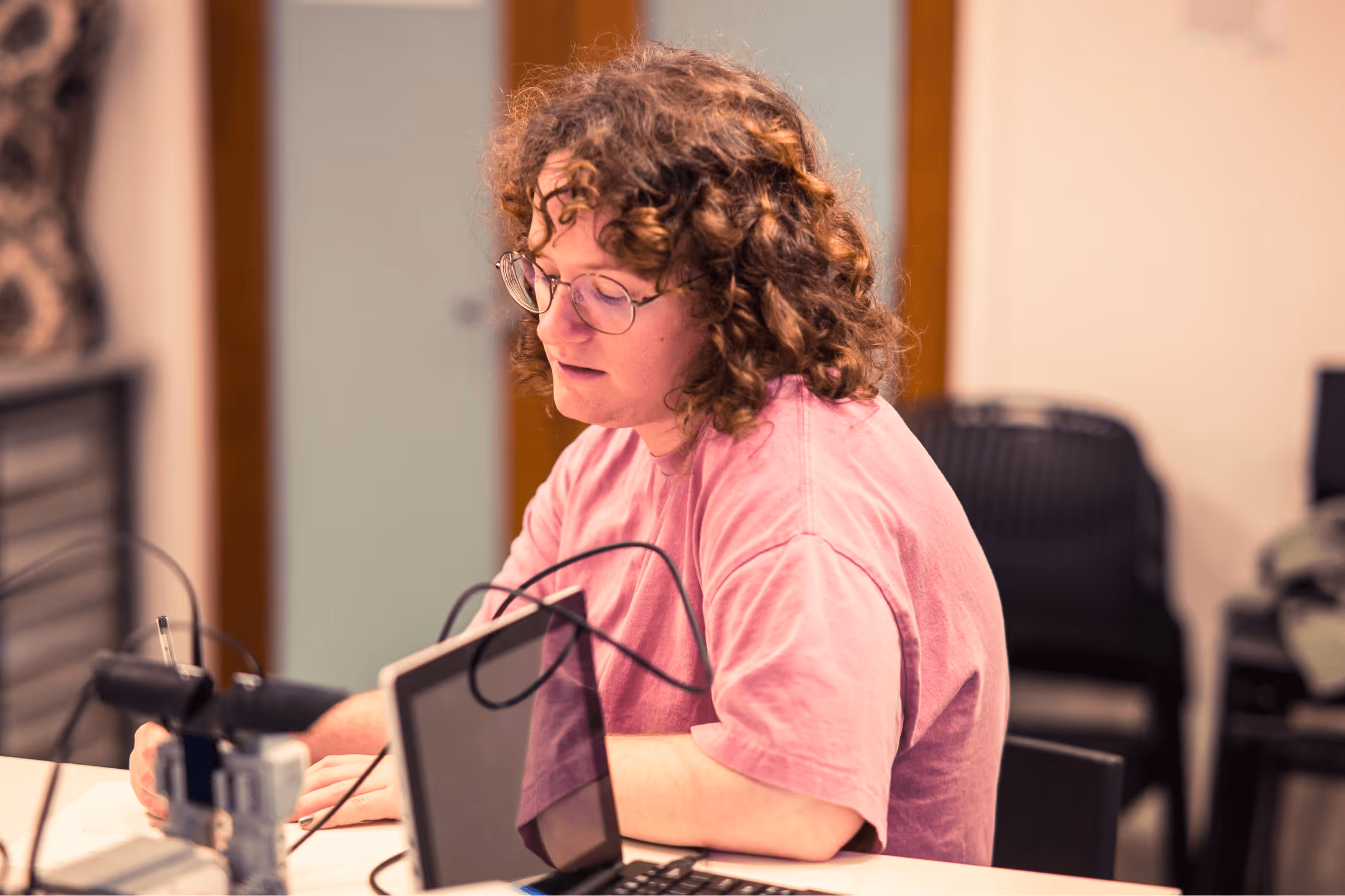 A young woman with autism and short, brown hair writing with a black pen at a white desk.