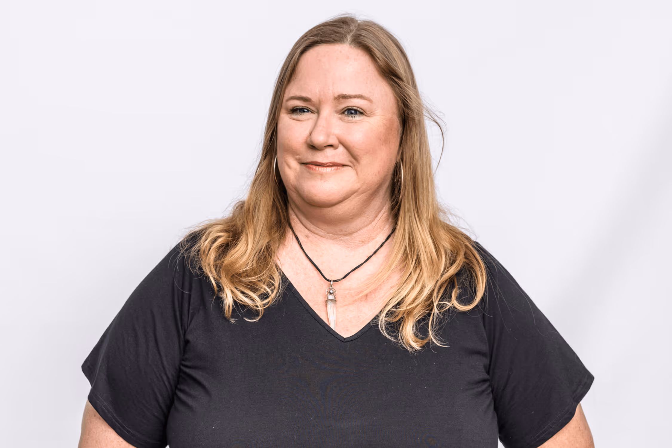 An autistic woman with shoulder-length blonde hair and a black t-shirt stands in front of a grey background.