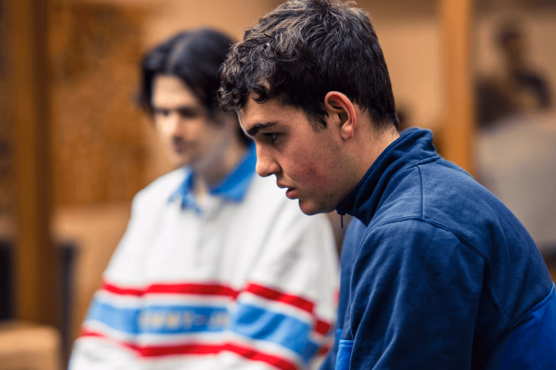 A young man with autism wearing a blue jacket staring at the ground looking upset.