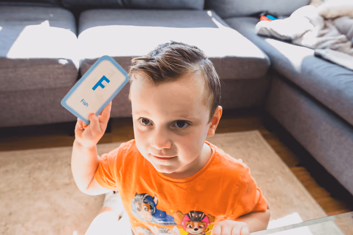 A young boy with short brown hair holding a card with the letter 'F' and the word 'Fish' written underneath.