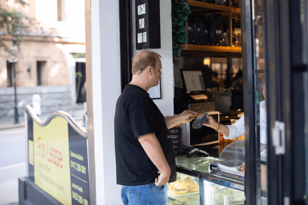 A young man with autism wearing a black shirt taps a yellow EFTPOS card onto a machine.