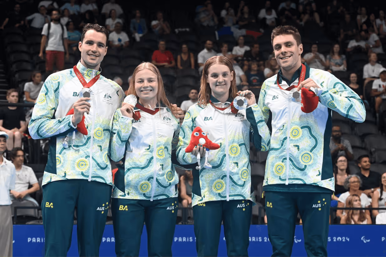 Four Paralympians standing together holding silver medals.