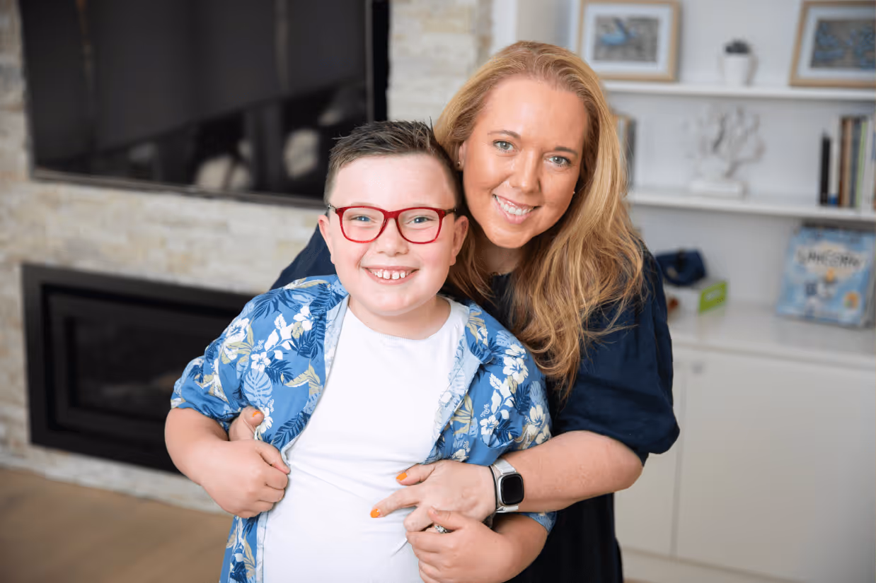 A mum with blonde hair hugging her son who is on the autism spectrum. He is wearing a Hawaiian shirt and red glasses and has short brown hair.