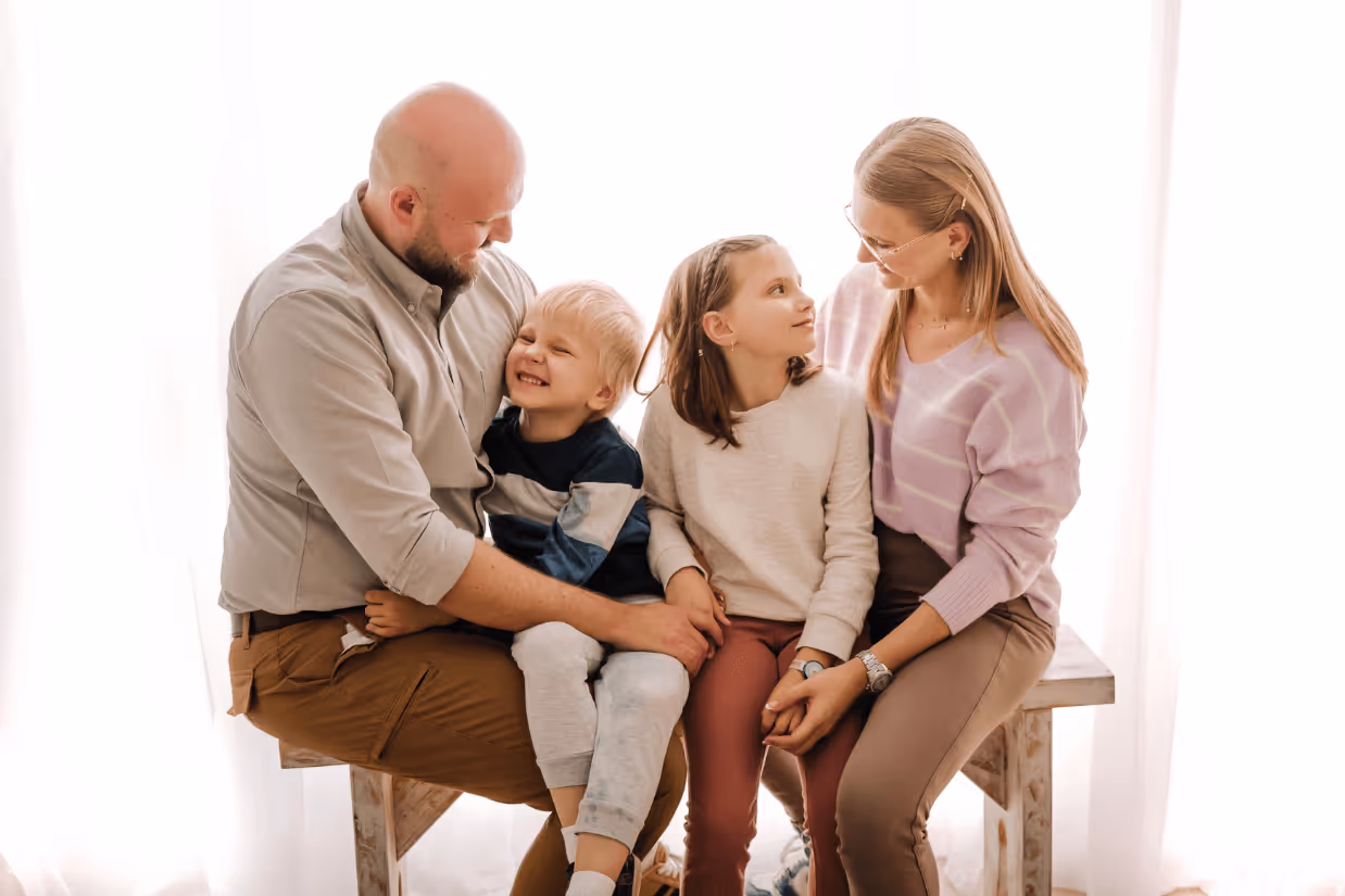 A family of four sit on a wooden bench and hug together.