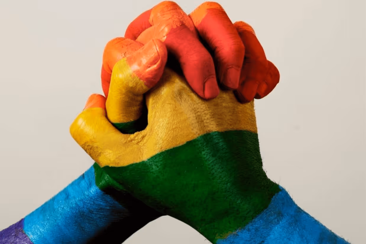 A pair of hands painted rainbow clasped together. 