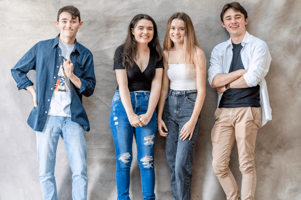A group of autistic and neurotypical teenagers smiling in front of a grey background.