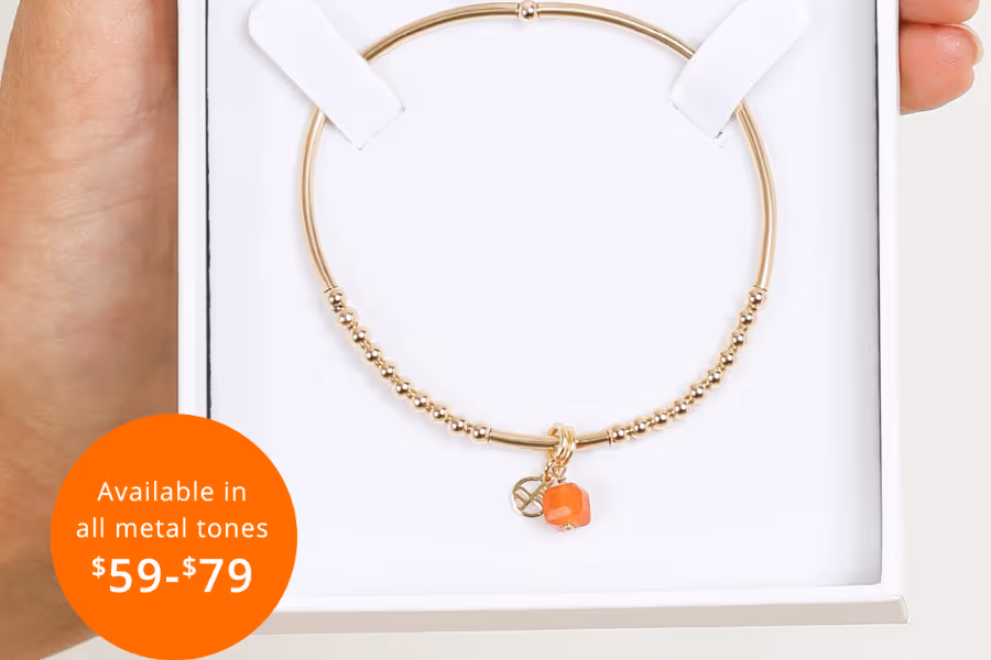 A gold bracelet with an orange charm and a circle next to it with the words 'Available in all metal tones - $59 - $79.