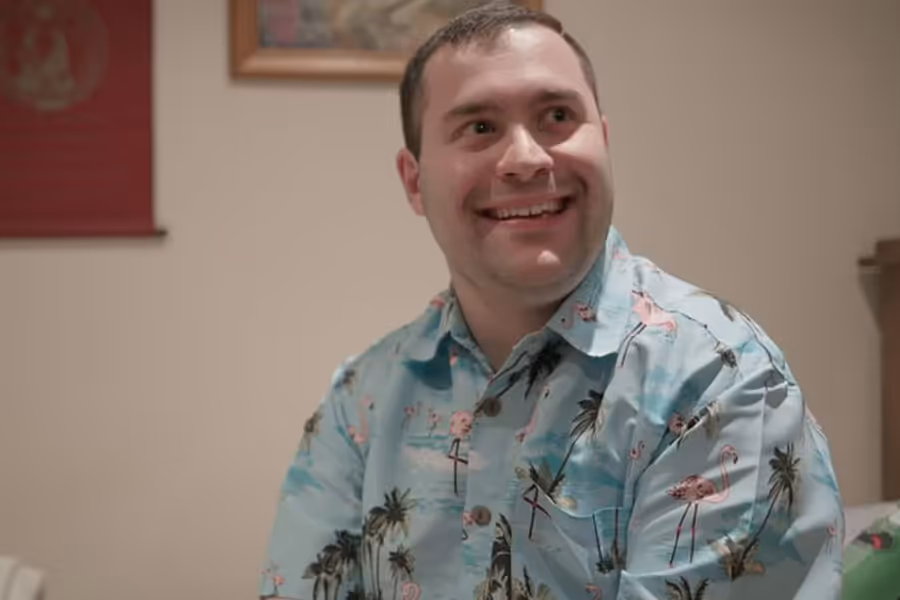 A young man with dark brown hair and a blue Hawaiian shirt smiling.