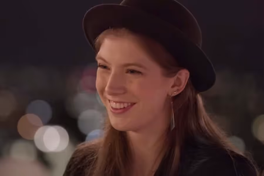 A young woman with autism with a black bowler hat and long brown hair smiling.