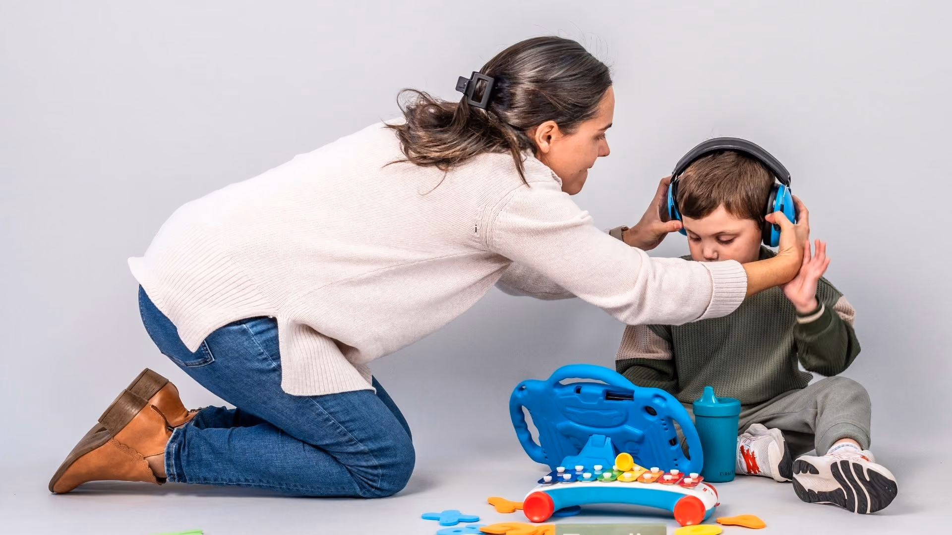 mother helping autistic child with ear defenders