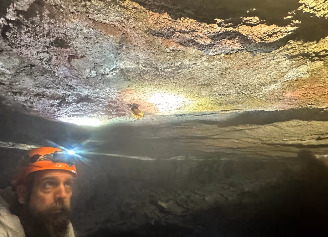 A Jefferson County Greenways staff member in a cave wearing a helmet with a headlamp and viewing a bat
