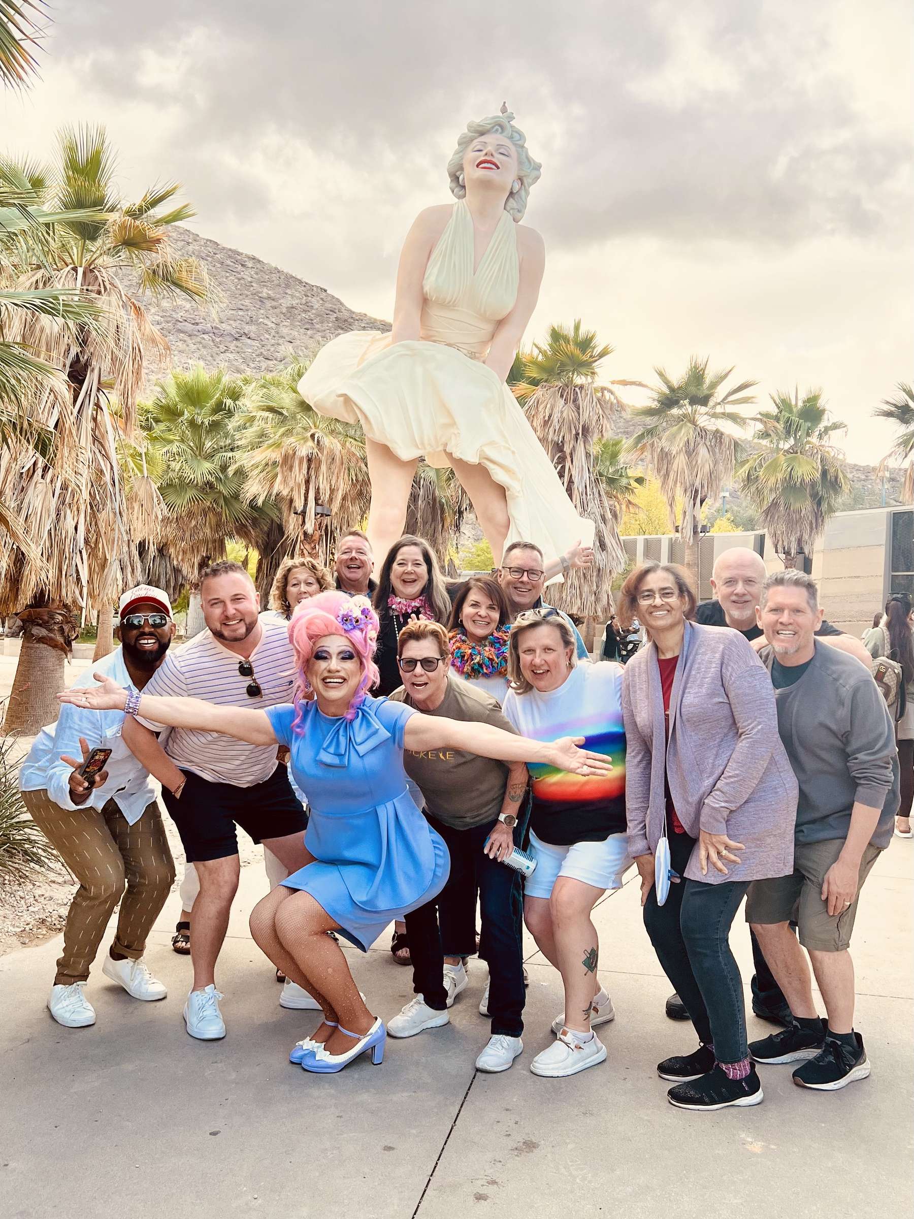 Anita Doll posing with a happy group of Drag & Fly Tours guests under the Forever Marilyn statue in Palm Springs