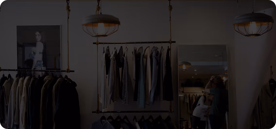 Clothing store interior with hanging garments, a large mirror reflecting shoppers, and modern pendant lights.