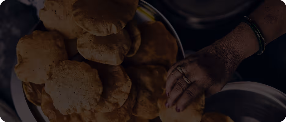 Close-up of a hand picking up a fried puffed bread from a plate filled with similar breads.