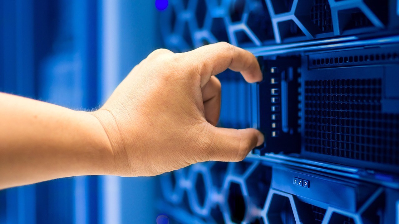 A hand slides a drive into a server rack, a reminder of the heavy computing power needed to train AI from scratch