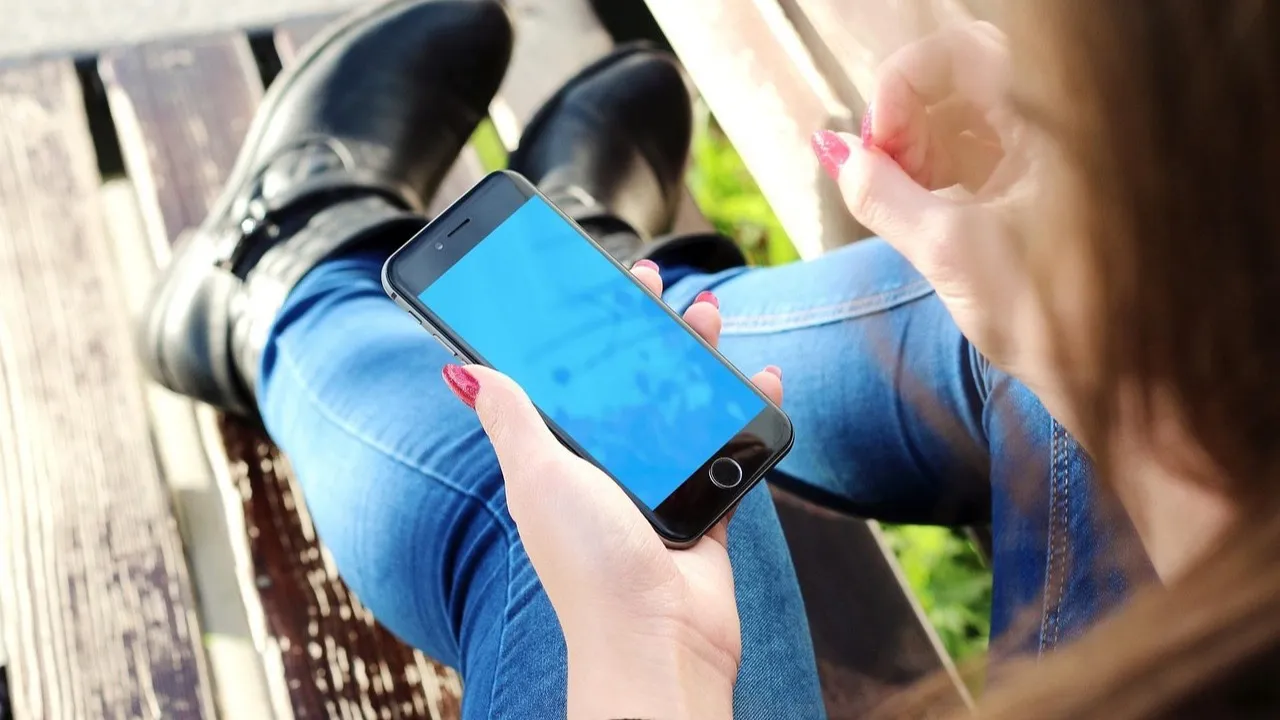 A woman holds a smartphone in one hand, trying out a simple new app idea on a real phone.